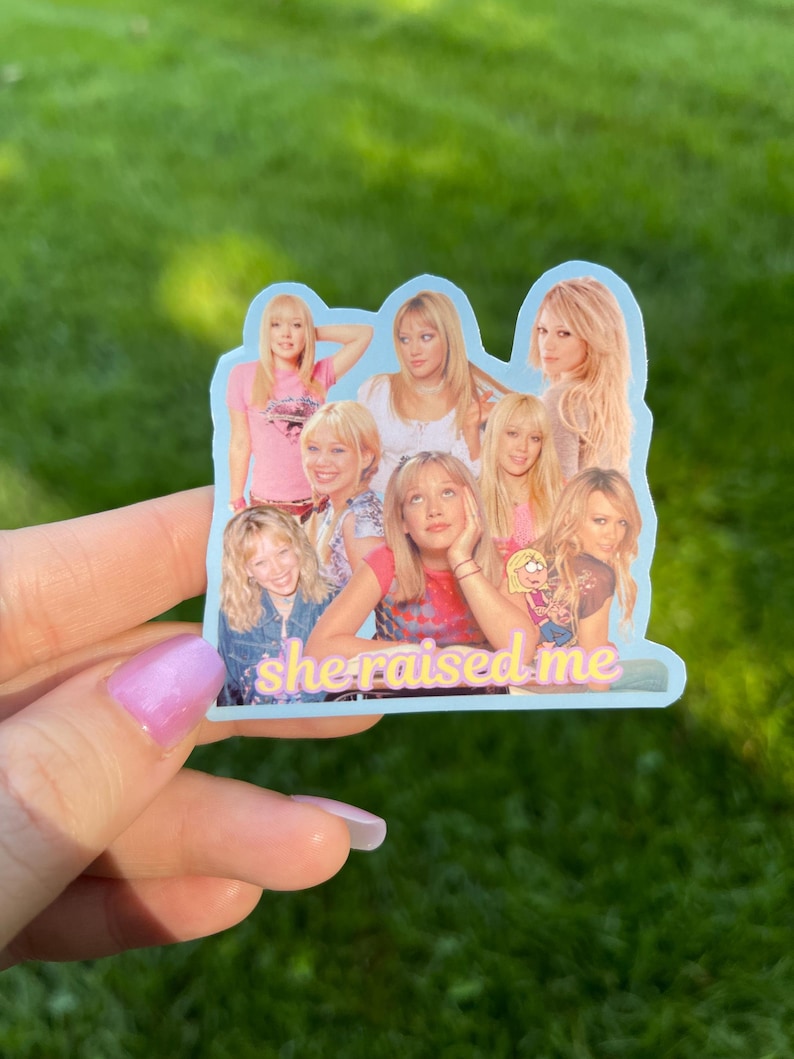 May include: A light blue sticker featuring a collage of images of a woman. The sticker has the text "she raised me" in a pink and yellow font. The background is green.