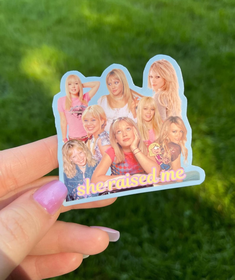May include: A light blue sticker featuring a collage of images of a blonde woman in various poses. The sticker has the text "she raised me" in a pink and yellow font.