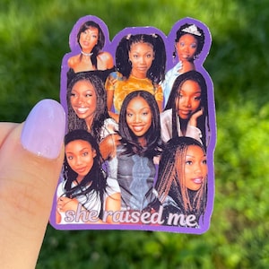 May include: A purple sticker featuring a collage of images of a woman. The sticker has a white border and the text "she raised me" in a script font. The background is a blurred green.