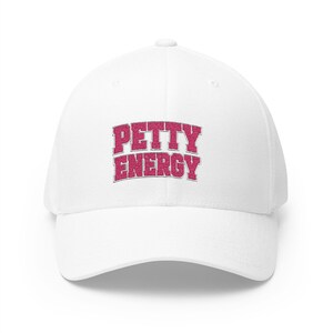 May include: White baseball cap featuring the embroidered phrase "PETTY ENERGY" in a pink, textured font. The cap has a curved peak and a structured fit, suitable for casual wear.
