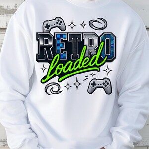 May include: White sweatshirt with the text "Retro Loaded" in a bold, black and blue design with a green cursive font. The design includes controller graphics and star accents, evoking a retro gaming theme.