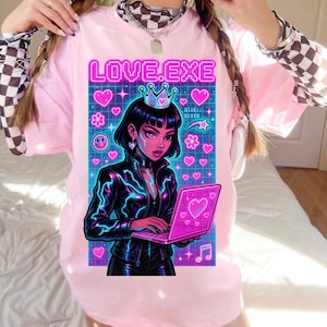 Op de afbeelding: Een lichtroze T-shirt met de tekst "LOVE.EXE" in neonroze. De afbeelding toont een vrouw met een kroon, die een roze laptop vasthoudt, omringd door harten, bloemen en sterren. De vrouw draagt een zwarte jas met neonblauwe accenten.