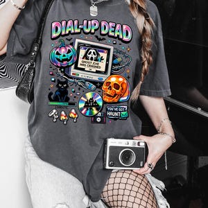 May include: Dark grey t-shirt featuring a colourful graphic with the text "DIAL-UP DEAD." The design includes a pumpkin, skull, computer screen, and a black cat. The text "GHOST.EXE HAS CRASHED" is on the screen.
