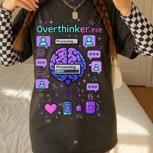 Puede incluir: Camiseta gris oscuro con el texto "Overthinker.exe" en verde azulado y morado. La camiseta presenta un gráfico de cerebro pixelado, bocadillos y un diseño de corazón, teléfono y taza de café. El diseño es en tonos morado, verde azulado y rosa.