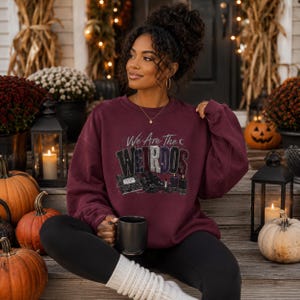 Puede incluir: Una sudadera de cuello redondo color granate con el texto We Are The Weirdos en una fuente estilizada, acompañada de ilustraciones gráficas de un cuaderno, botas, pintalabios y velas. Se lleva con leggings negros y calentadores blancos.
