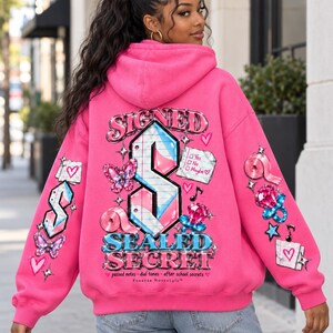 May include: A bright pink hooded sweatshirt featuring a large graphic on the back with the text SIGNED SEALED SECRET, a stylised letter S, a butterfly, a note with checkboxes, and a dummy. The sleeves also feature matching graphic prints.