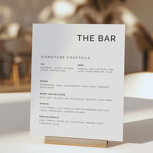 May include: A white sign with black text listing the bar menu. The sign reads "The Bar" at the top and lists signature cocktails, wines, beers and seltzers, spirits, and non-alcoholic drinks.
