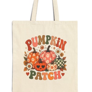 Peut inclure: Un sac fourre-tout en toile couleur crème avec une impression graphique portant le texte PUMPKIN PATCH en orange, marron et vert. Le motif comprend cinq citrouilles aux motifs variés, dont des carreaux et des fleurs, entourées de petites fleurs et de cœurs.
