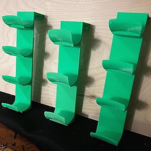 Op de afbeelding: Drie heldergroene wandopslagrekken. Elk rek heeft een rechthoekige achterkant en drie gebogen planken. De rekken zijn gemonteerd op een lichtgekleurd houten oppervlak. De planken zijn ontworpen om items vast te houden.