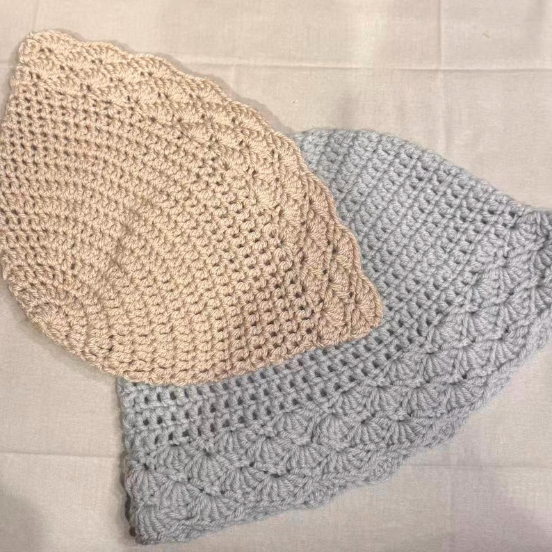 May include: Two crocheted items, one beige and one light blue, are displayed. Both have a scalloped edge and a textured, open weave pattern. The items appear to be handmade, possibly dishcloths or decorative pieces.