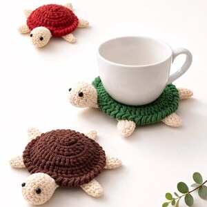 Könnte beinhalten: Gehäkelte Schildkröten-Untersetzer in Rot, Grün und Braun. Jeder Untersetzer hat ein Schildkröten-Design mit rundem Panzer, Kopf und Füßen. Eine weiße Tasse steht auf dem grünen Schildkröten-Untersetzer.