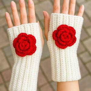 May include: A pair of ivory-colored, knitted fingerless gloves, each adorned with a vibrant red rose applique. The gloves are designed to keep hands warm while leaving fingers free. The rose is a prominent decorative element.