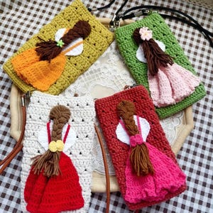 Puede incluir: Cuatro bolsos de ganchillo con un diseño de muñeca. Los bolsos son de diferentes colores: verde, naranja, blanco y rosa. Cada bolso tiene una correa marrón.