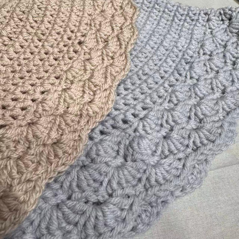 May include: Close-up of two crocheted blankets. One is a light beige color, and the other is a light gray. Both blankets have a textured, scalloped edge and a repeating pattern of raised stitches, creating a cozy, handmade appearance.