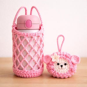 May include: A pink insulated water bottle in a crocheted carrier with a matching pink sheep-shaped keychain. The carrier has a diamond-patterned net design and a handle. The keychain has a white face, pink ears, and a flower.