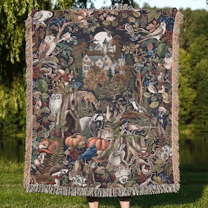 May include: A tapestry blanket depicting a forest scene with owls, deer, and rabbits. The central design features a castle and moon. The blanket has a dark background and a fringed edge, with a detailed woodland design.