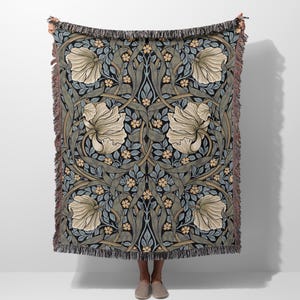 Peut inclure: Une couverture en tissu tissé avec un motif floral dans des tons de bleu, vert et beige. Le motif présente des fleurs et des feuilles stylisées.