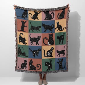 Puede incluir: Una manta tejida con un diseño de patchwork colorido que presenta siluetas negras de gatos con patrones de estrellas. Los gatos están en varias poses, incluyendo sentados, de pie y acostados.