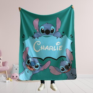 Op de afbeelding: Een tealblauwe fleece deken met een cartoon Stitch-personage uit Lilo & Stitch. De deken heeft drie Stitch-personages met een spraakballon die "Charlie" zegt.
