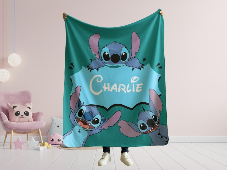 Op de afbeelding: Een tealblauwe fleece deken met een cartoon Stitch-personage uit Lilo & Stitch. De deken heeft drie Stitch-personages met een spraakballon die "Charlie" zegt.