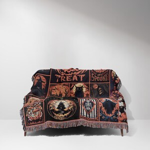May include: A black and orange Halloween-themed throw blanket draped over a couch. The blanket features various spooky illustrations, including a pumpkin, a skeleton, and a black cat. The words "TREAT and SPOOKY" are also visible on the blanket.