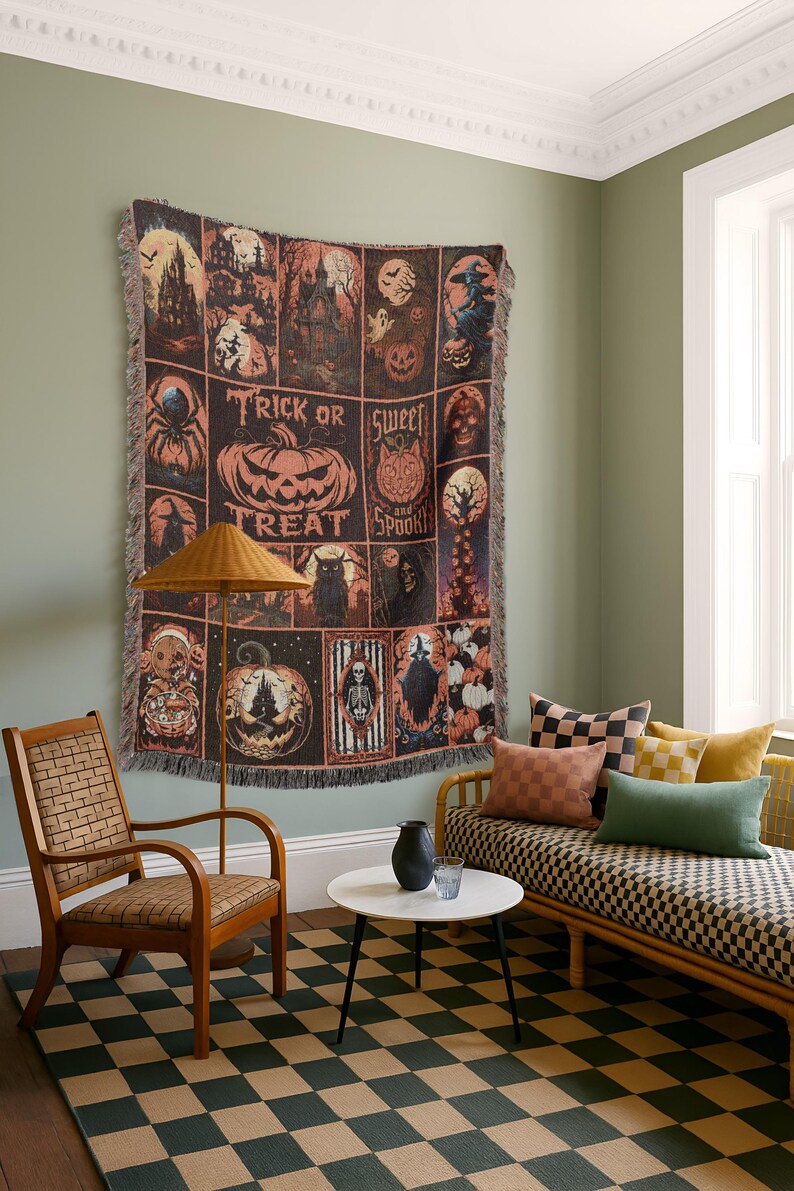 May include: A Halloween-themed throw blanket with a grid pattern featuring spooky illustrations and the words "Trick or Treat" and "Sweet and Spooky". The blanket is displayed on a wall in a room with a chair, couch, and checkered rug.