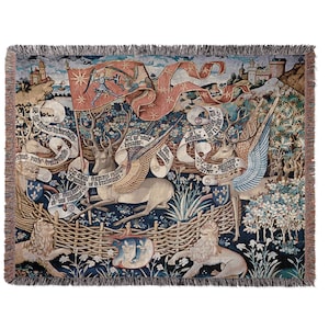 May include: Woven tapestry throw blanket featuring a medieval scene with winged deer, lions, and a castle. The design includes a red banner with a knight and text, set against a dark blue background with a woven fringe.
