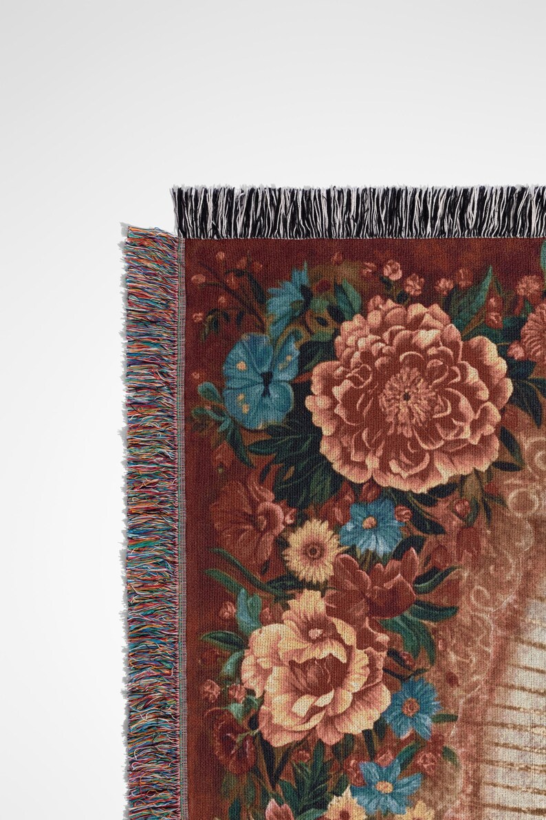 May include: A woven throw blanket featuring a floral design in shades of brown, orange, and blue. The blanket has a fringed edge with a mix of colors. The design includes large flowers and smaller floral accents.