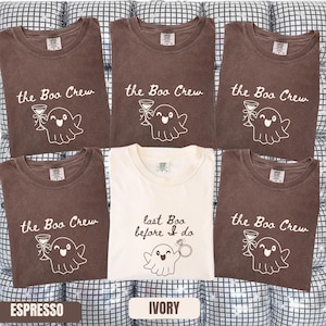 May include: Five t-shirts arranged in a grid. Four are espresso brown with white text reading the Boo Crew and a ghost holding a martini glass. One center t-shirt is ivory with brown text reading last Boo before I do and a ghost holding a ring.