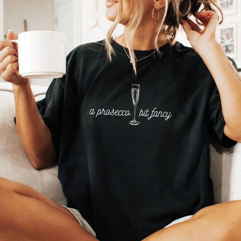 May include: Black t-shirt with a white graphic of a champagne flute and the text "a prosecco bit fancy".