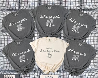 May include: A collection of gray and ivory t-shirts. The gray shirts have the text "Let's go girls" with a cowboy boot graphic. The ivory shirt says "man, I feel like a bride" with a ring graphic. The shirts are labeled "Pepper" and "Ivory".