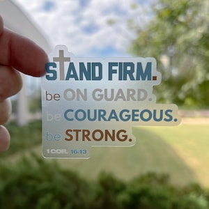 May include: A clear sticker with a cross and the text "STAND FIRM. be ON GUARD. be COURAGEOUS. be STRONG. 1COR 16:13"