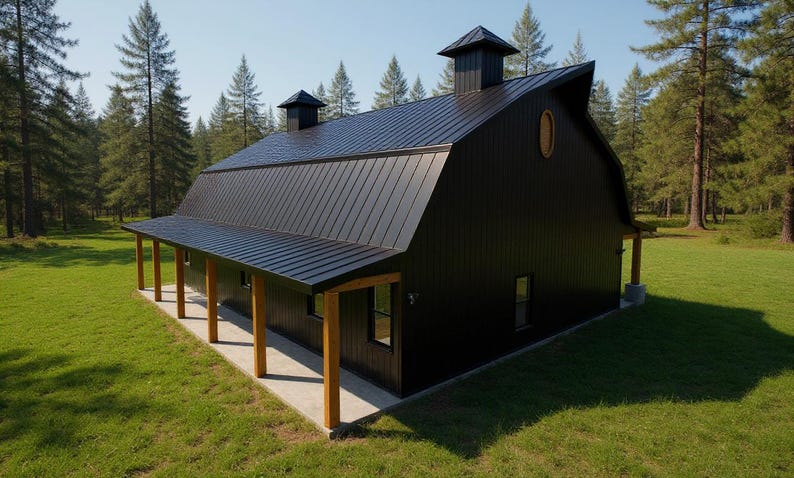 May include: A black barn-style building with a metal roof, two cupolas, and a covered porch supported by wooden posts. The structure features vertical siding, rectangular windows, and an oval window on the upper gable end, set in a grassy area.
