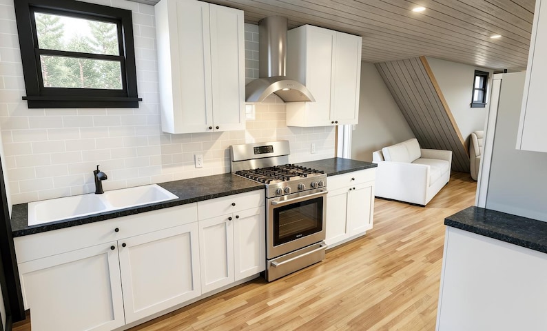 May include: A modern kitchen with white cabinets, a stainless steel stove and range hood, and a black countertop. The kitchen has a white sink and a window with a black frame. The flooring is light-colored wood.