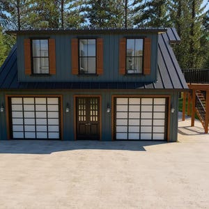 May include: A two-story building with a dark blue exterior, three windows with brown shutters, and two garage doors with a grid pattern. A wooden staircase leads to a small balcony. The building is surrounded by trees and a concrete driveway.