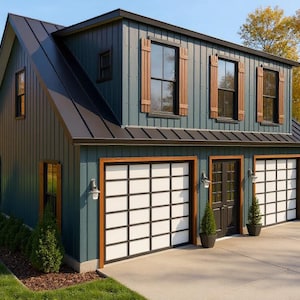May include: A two-story teal-colored garage with a black roof and brown trim. The garage has two garage doors with white panels and black grid patterns, and a single door. The building is surrounded by green grass and trees with yellow leaves.