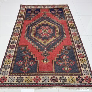 May include: A rectangular area rug featuring a central diamond medallion in dark blue and gold on a vibrant red field. The border displays a repeating floral pattern in red, gold, and blue, finished with short fringe along the top and bottom edges.