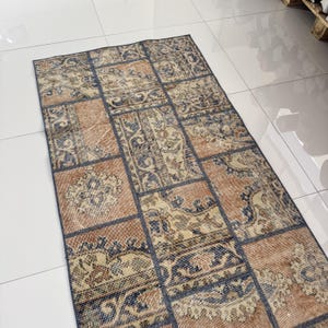 May include: A rectangular patchwork rug with a distressed, vintage look. The rug combines muted orange, beige, and navy blue hues. The design is made up of rectangular patches with floral and geometric patterns.