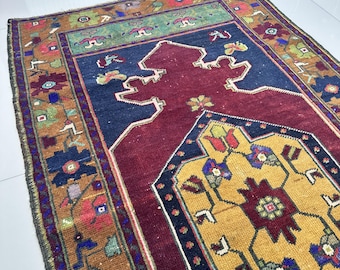 May include: A rectangular, vintage rug with an intricate, floral pattern. The rug features a central maroon field, bordered by navy blue, gold, and green sections. The edges are adorned with a detailed, multi-colored floral design.