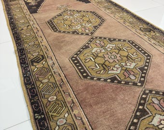 Könnte beinhalten: Ein rechteckiger Vintage-Teppich mit verblichenem Aussehen. Der Teppich hat ein zentrales Feld in gedämpftem Rosé, mit geometrischen Mustern in Olivgrün, Schwarz und Creme. Der Rand hat ein sich wiederholendes Design.