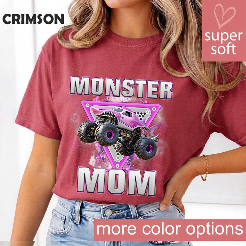 May include: Crimson red t-shirt with the words "MONSTER MOM" in silver block letters. A pink monster truck with a shark mouth design is centered on a pink triangle. The words "super soft" and "more color options" are also visible.