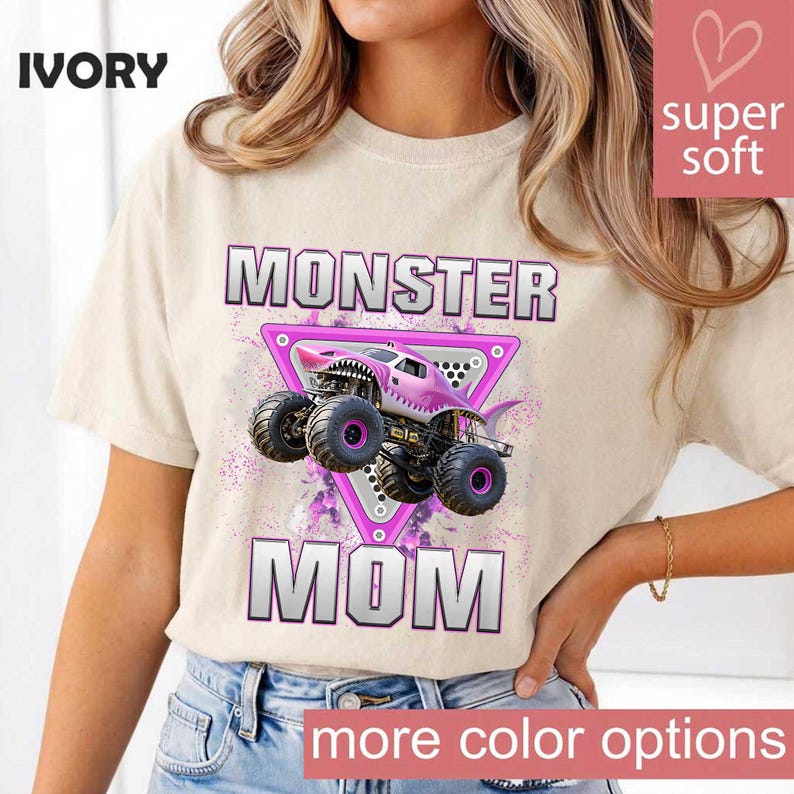 May include: Ivory-colored t-shirt with the words "MONSTER MOM" in a bold, outlined font. A pink monster truck graphic is centered within a pink triangle. The shirt also has the words "super soft" and "more color options".