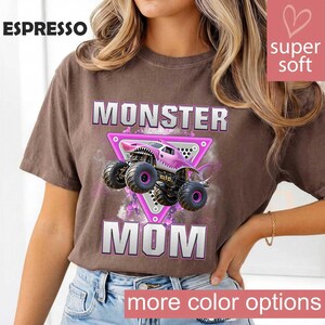 May include: Espresso-colored t-shirt featuring a pink monster truck design with the words "MONSTER MOM." The graphic includes a pink triangle and the text "super soft." The shirt has a relaxed fit and is made of soft material.