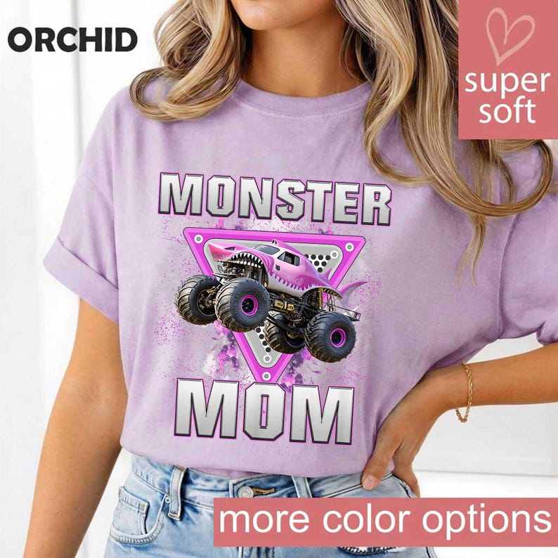May include: A light purple t-shirt with the words "MONSTER MOM" in silver block letters. A pink monster truck graphic is centered between the words. The shirt has the word "ORCHID" at the top left and "super soft" in a pink heart-shaped box.
