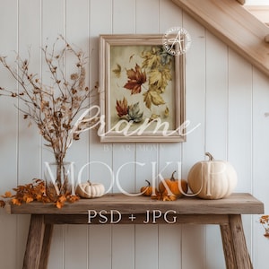 Peut inclure: Une table en bois rustique présente une décoration d'automne. Une œuvre d'art encadrée avec des feuilles d'automne est suspendue au-dessus de citrouilles et d'un vase de branches séchées. Le texte "Frame" et "Mockup" est inclus.
