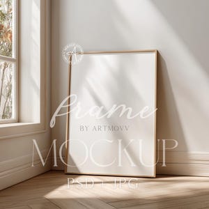 Könnte beinhalten: Ein großer, rechteckiger, leerer Bilderrahmen mit hellem Holzfinish lehnt in einer sonnigen Ecke an einer Wand. Der Rahmen steht auf einem Holzboden, mit dem Text "Frame by ARTMOV" und "MOCKUP PSD + JPG" sichtbar.