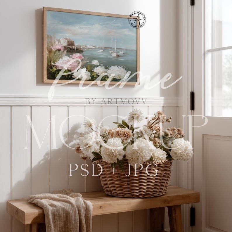 May include: A framed landscape painting depicting a coastal scene with sailboats and buildings, hanging above a wooden bench. A wicker basket filled with white and tan flowers sits on the bench, with a folded beige blanket. The image is a mockup, with the text "Frame by Artmovv" and "PSD + JPG".