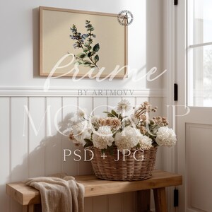 May include: A framed botanical print featuring blue and green flowers hangs above a wooden bench. A woven basket filled with white and tan flowers sits on the bench, with a folded beige blanket. The image is a mockup.