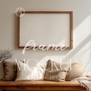 Puede incluir: Un marco de fotos rectangular de madera cuelga de una pared neutra sobre un banco de madera. Debajo hay tres almohadas en tonos beige y marrón. La palabra "Frame" está escrita en cursiva.