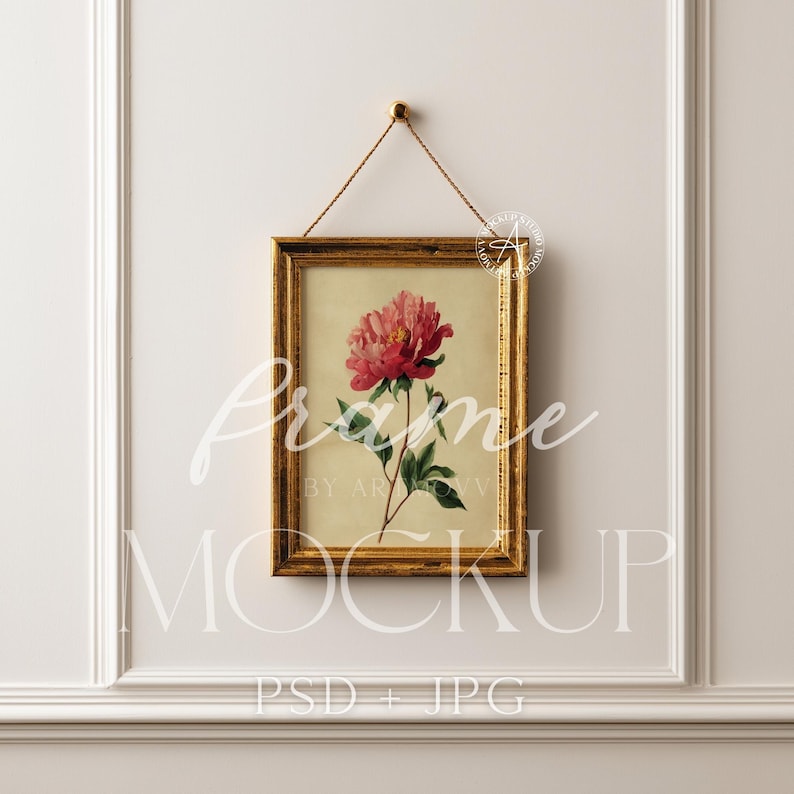 Pu&ograve; includere: Una stampa floreale incorniciata con una peonia rosa con foglie verdi, su sfondo crema. La cornice dorata &egrave; sospesa da un sottile cordino dorato. Le parole "Frame Mockup" e "PSD + JPG" sono visibili.